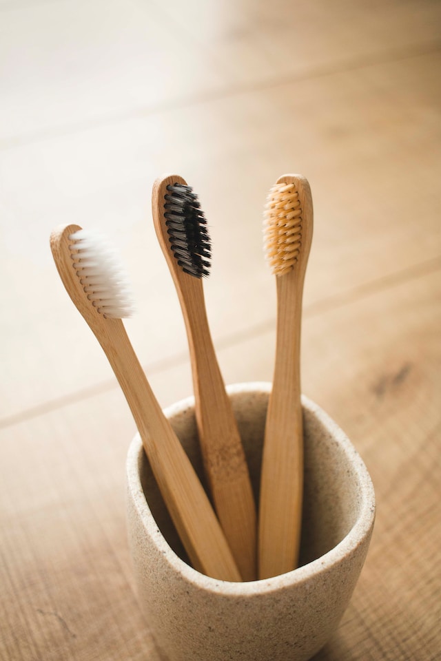 Three wooden toothbrushes inside a cup, on a table.